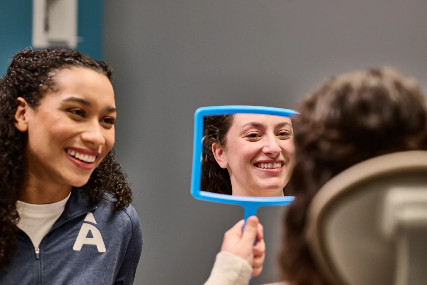 An Aspen Dental patient smiles into a handheld mirror. 