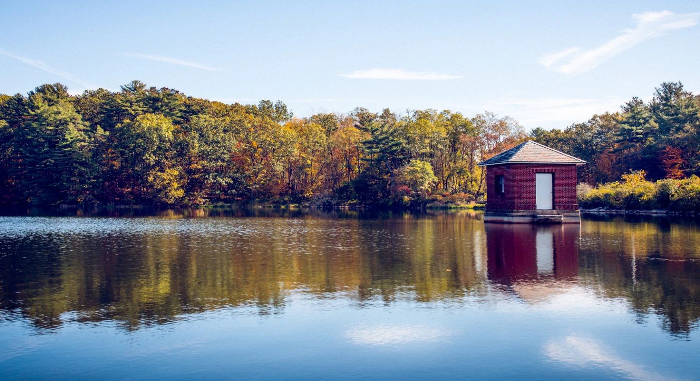 A view of a small red building on a lake surrounded by fall foliage