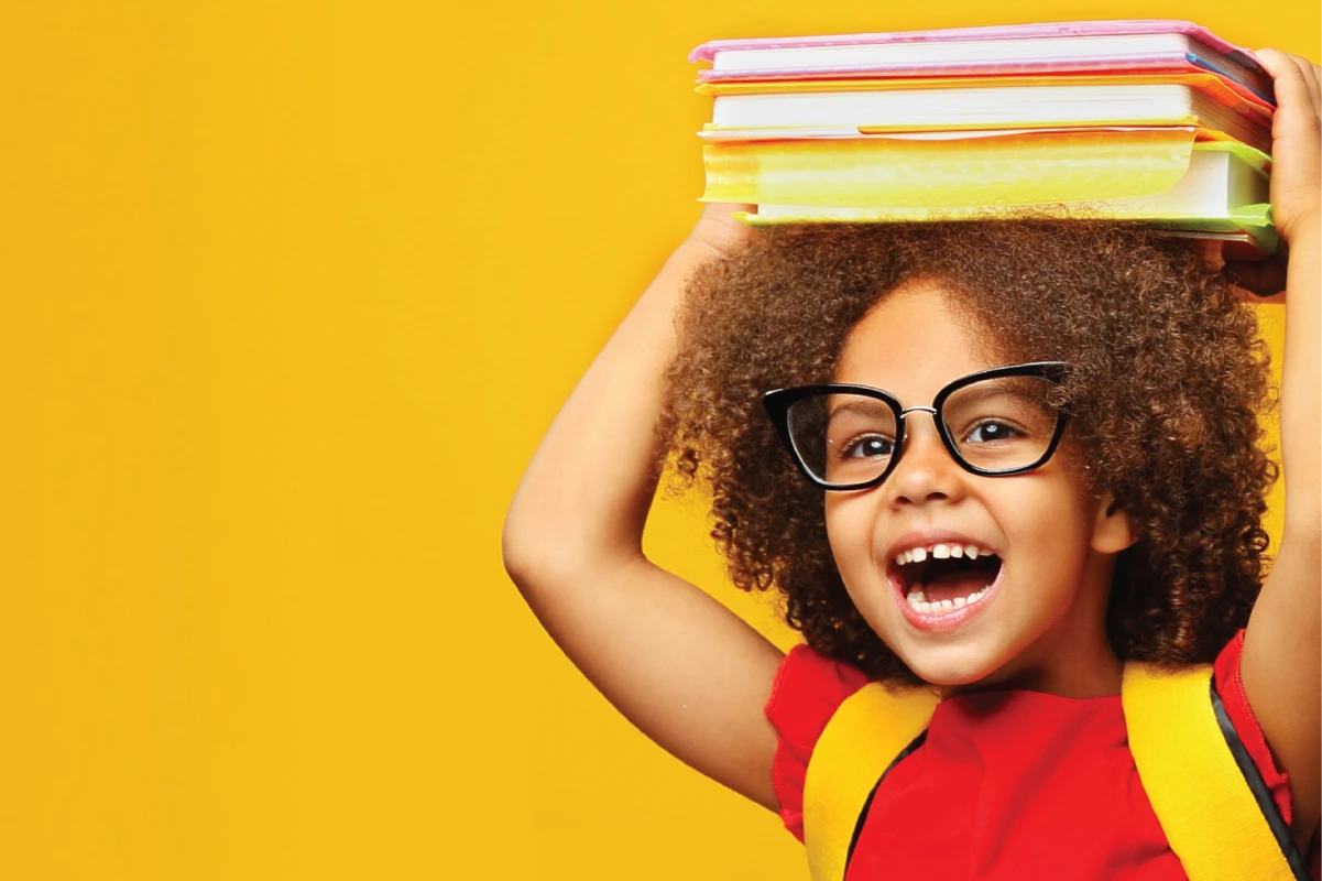 A young girl smiles as she stacks schoolbooks on her head. 