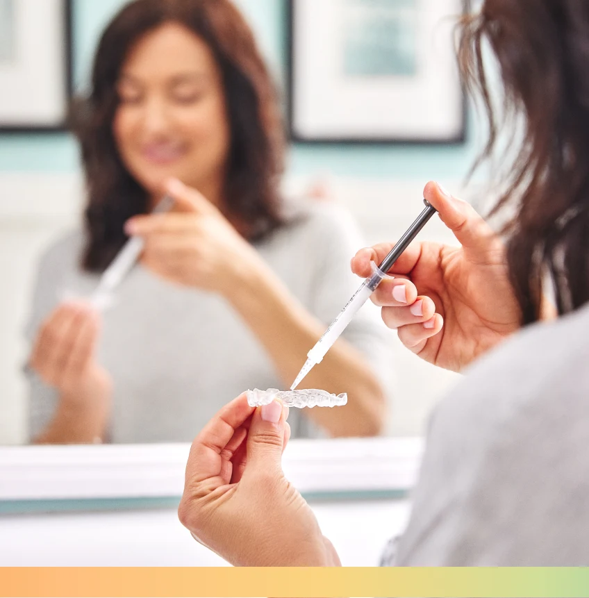 A person is holding a dental aligner in one hand and a syringe in the other, while standing in front of a mirror.