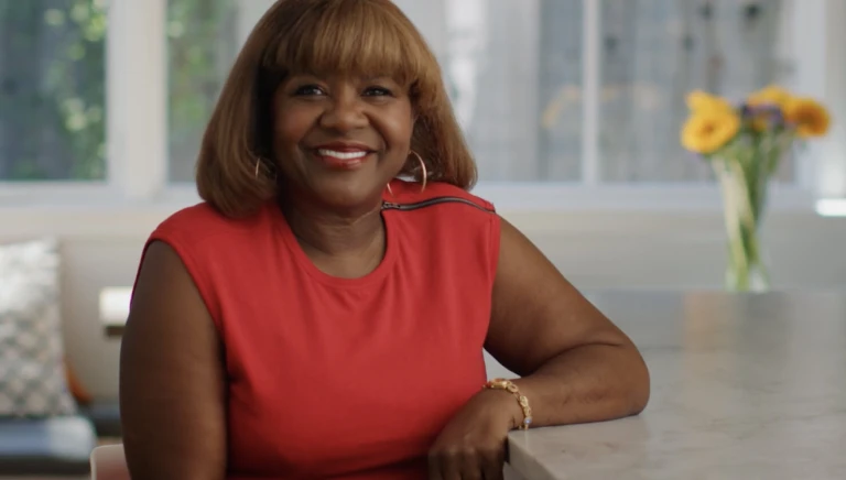 A woman smiles as she sits at a table while looking into the camera