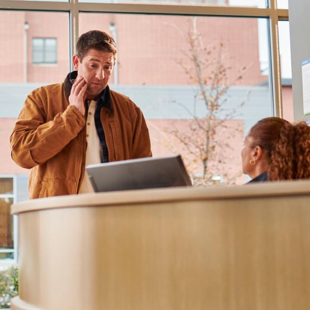 A patient with tooth discomfort speaking to a staff member at the reception desk at Aspen Dental.