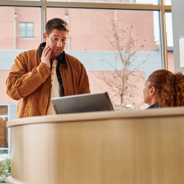A patient with tooth discomfort speaking to a staff member at the reception desk at Aspen Dental.