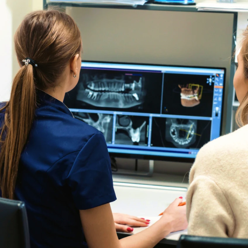 Dental assistant and a patient reviewing dental x-rays on a computer.