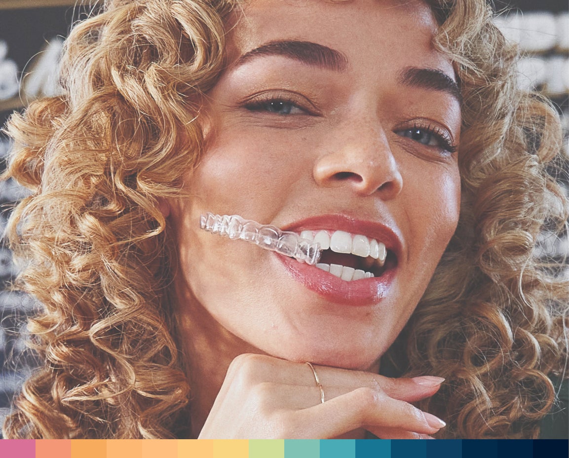 Close-up of a smiling woman with curly hair wearing a clear aligners.