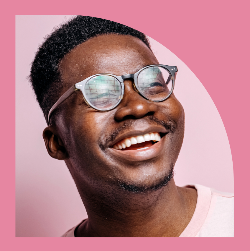 A person with glasses, wearing a light pink shirt, smiles and looks off to the side against a pink background.
