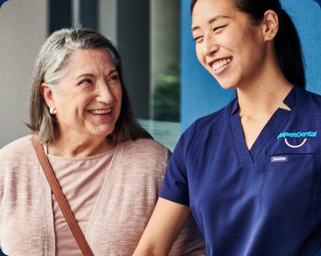 An elderly woman smiling and holding a conversation with a female dental professional, who is also smiling, both standing indoors. Text at the bottom reads, "Address issues promptly".