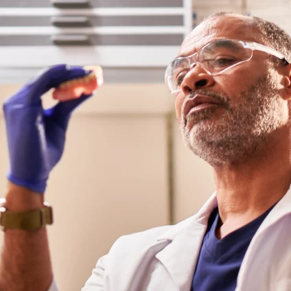 A dental lab technician analyzes a pair of dentures for any visible cracks or damage, representing a dental emergency situation.