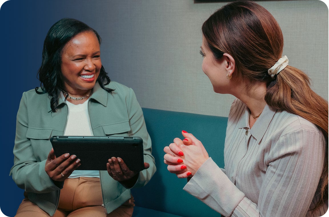 A female ClearChoice employee in a light grey long sleeve providing a female patient, who is wearing a white shirt and a green jacket, with payment options and potential discounts to make dental implant payments more manageable.