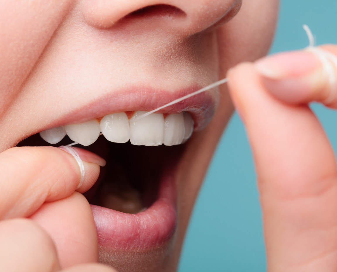 Close-up of a person flossing their white teeth with dental floss.