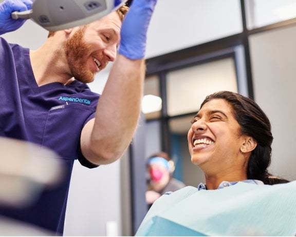 An Aspen Dental dentist talking to a patient in a dental chair.