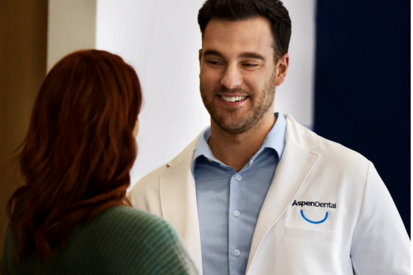 An Aspen Dental dentist in a white coat is conversing with a patient about her oral health.