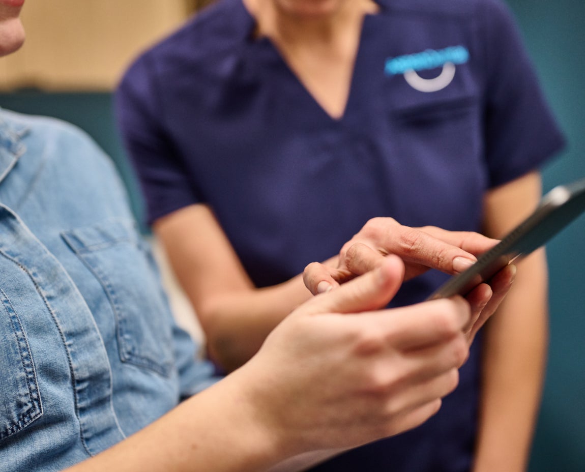 Two people standing close together, one in a blue shirt and the other in a navy uniform, while looking at and pointing to a tablet screen.