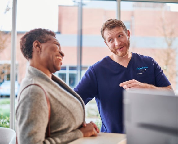 An Aspen Dental professional in a blue uniform smiling and engaging warmly with a patient during a consultation at the clinic.