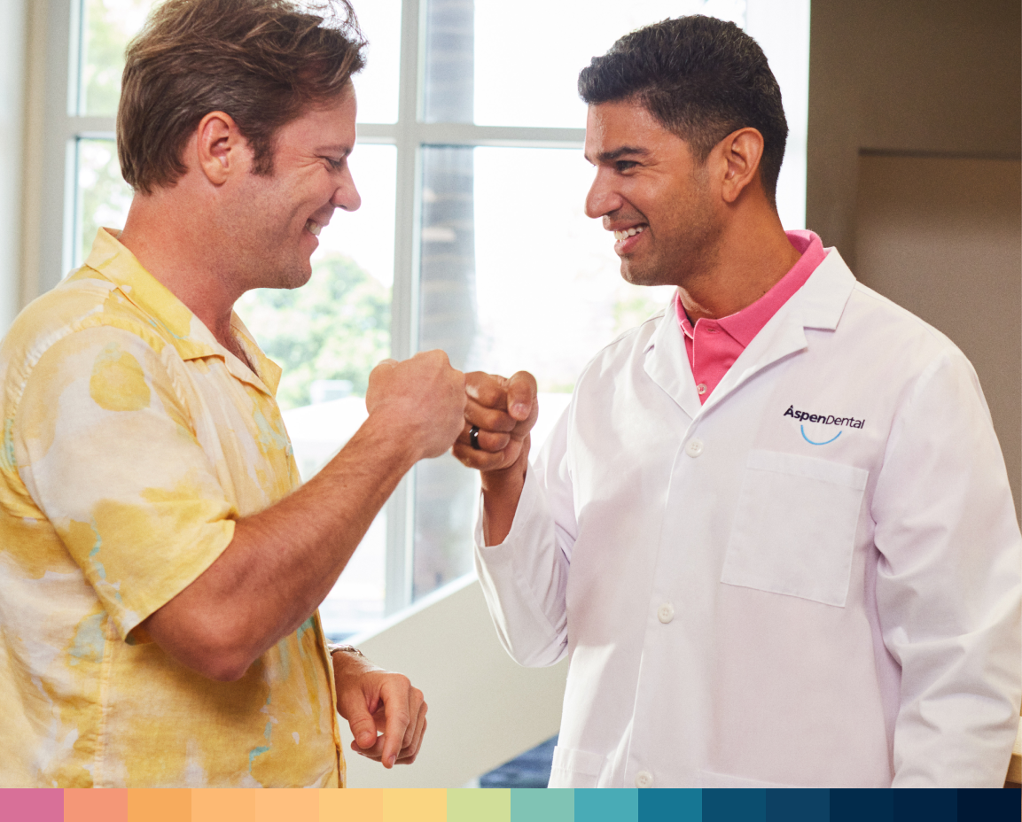 Dental specialist and patient smiling and fist bumping in dentist office.