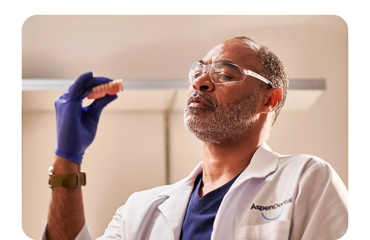 Aspen Dental professional inspecting dentures closely during on-site reline service, ensuring quality and efficiency for patients.