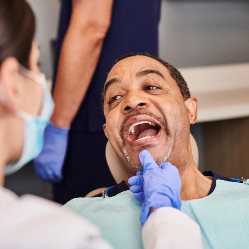 entist examining smiling male patient's teeth during periodontal treatment.