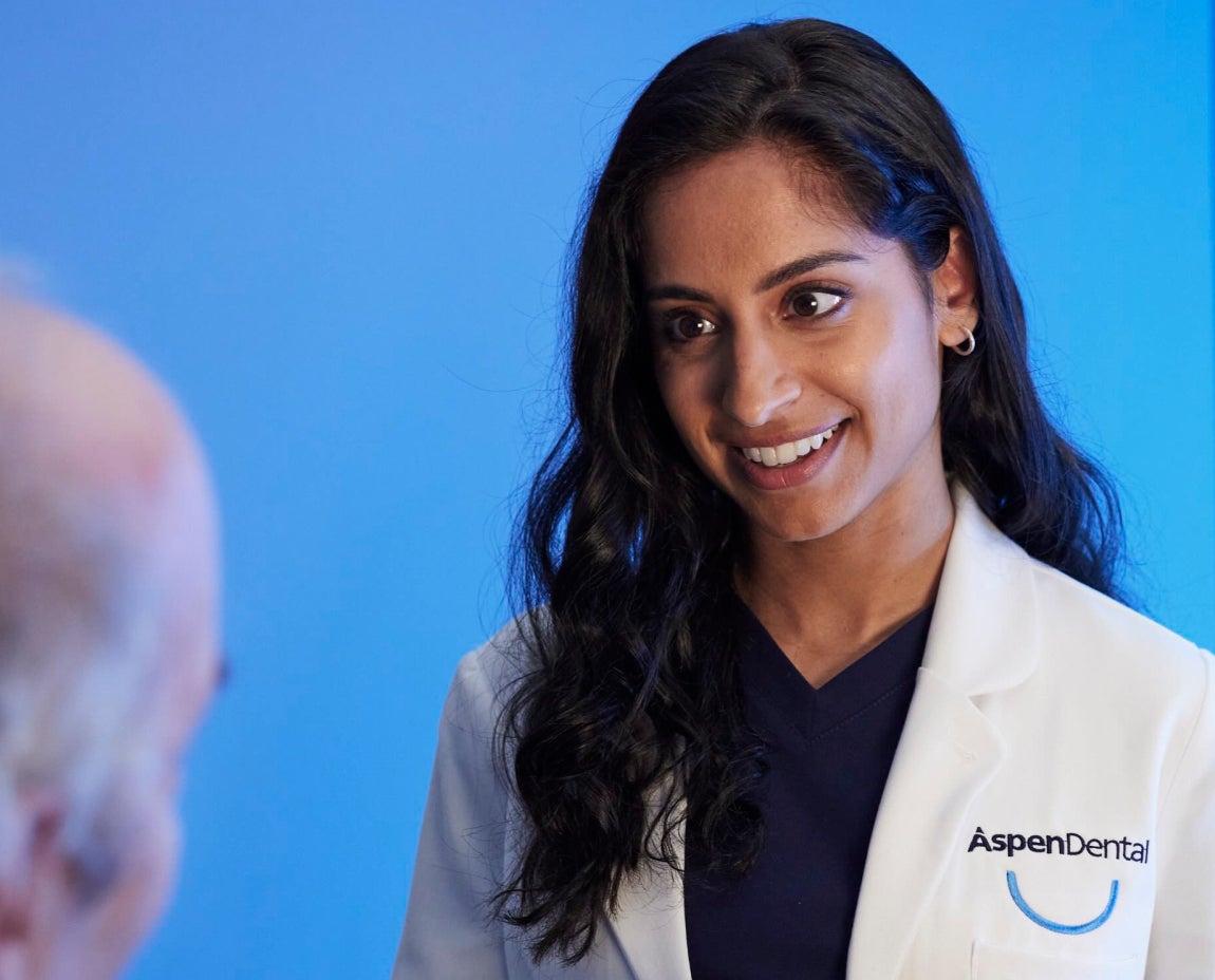  Female Aspen Dental professional smiling while consulting with a patient, providing dental care advice in a welcoming environment.