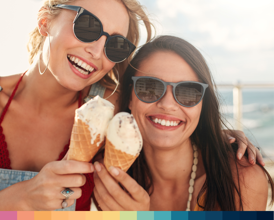 Two happy women in sunglasses enjoying ice cream at the beach.