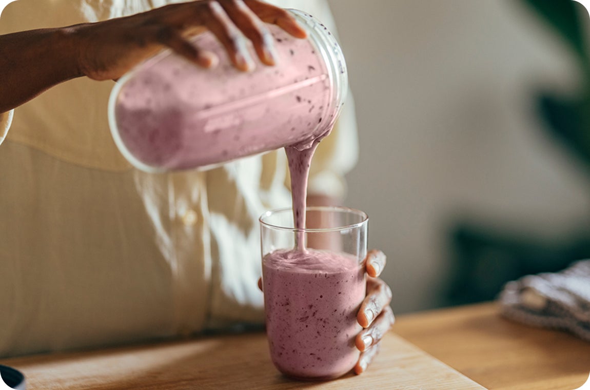 A patient pouring pink smoothie from a blender cup into a cooler glass, as they are following a soft, liquid diet to help ensure a safe and speedy healing process after their dental implant treatment.