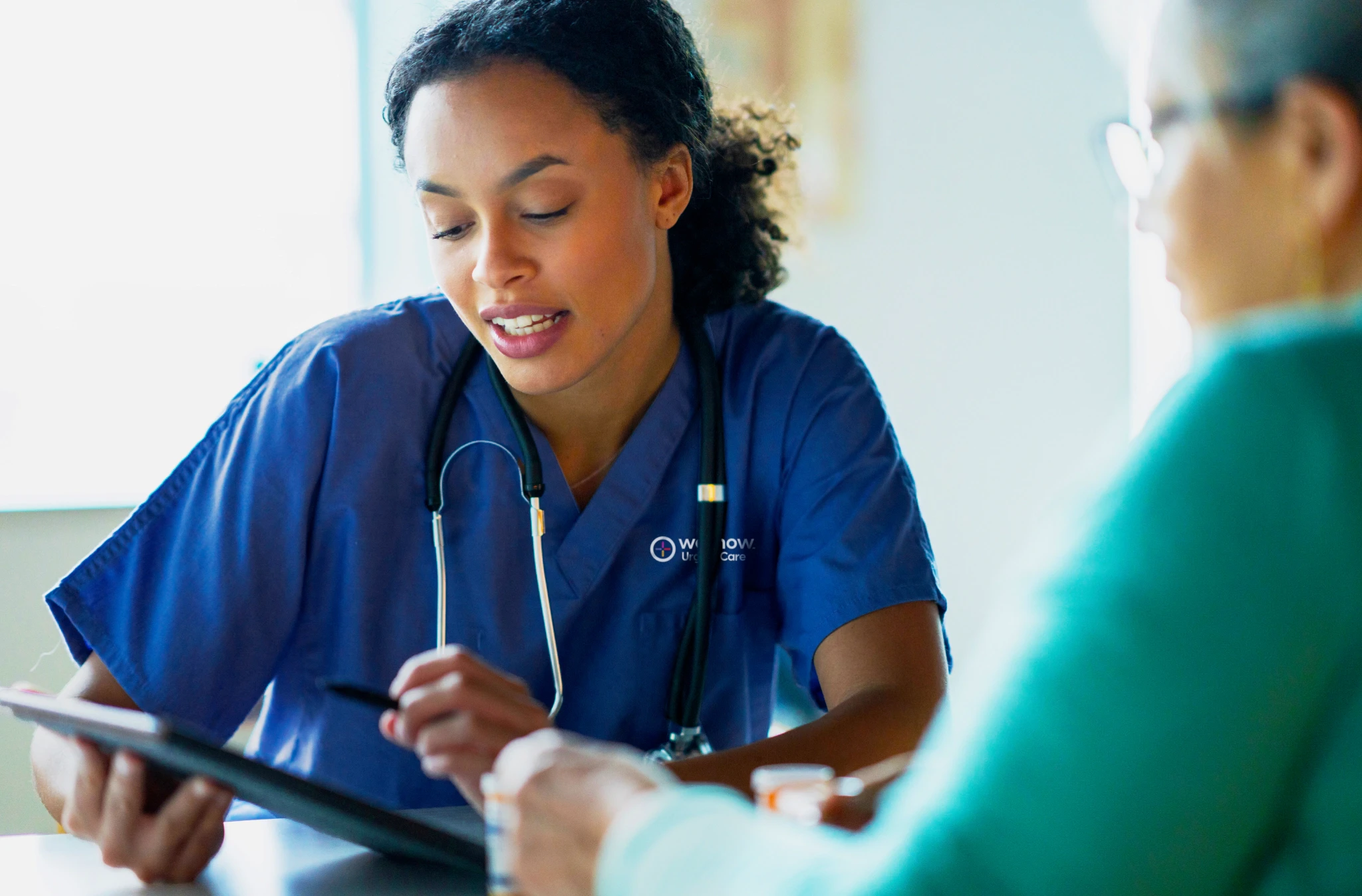 A WellNow doctor discusses with a patient while motioning to a tablet with a stylus.