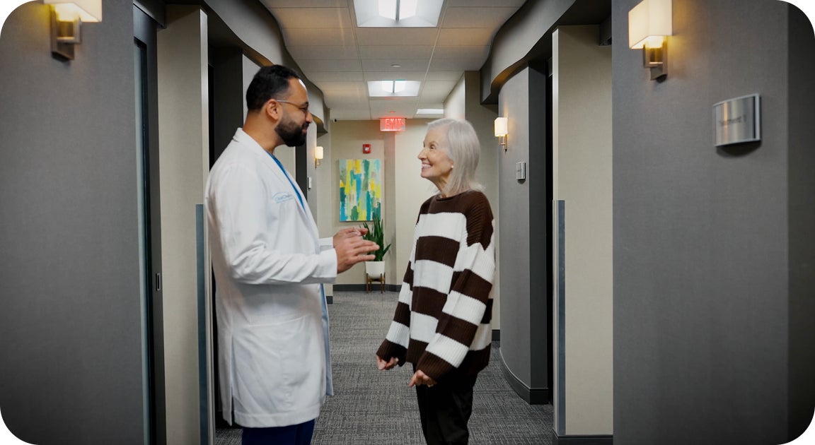 A ClearChoice doctor in a white lab coat, talking to an older patient in a center hallway, after she has completed her dental implants treatment and received her new, customized smile.