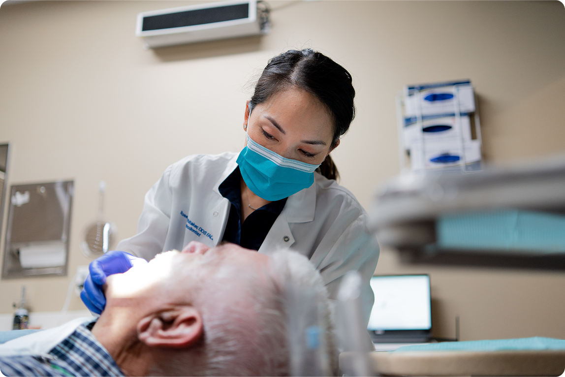 A ClearChoice dentist wearing a mask and gloves examining a patient in a treatment room, demonstrating attentive care during a dental implant appointment.
