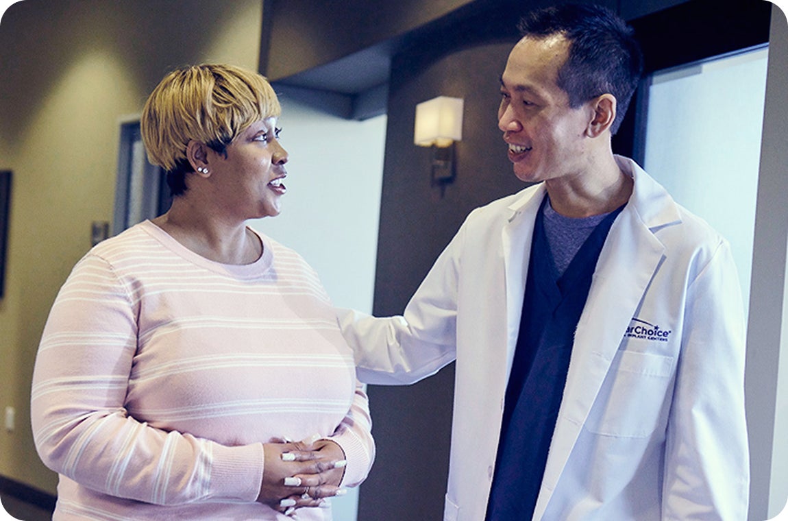 A ClearChoice prosthodontist in a white lab coat walking his patient, a woman in a pink stripe long sleeve, out of a center, after helping her explore third-party financing options and exclusive ClearChoice offerings such as the Insurance Assurance and Lifetime zirconia warranties for her dental implants.