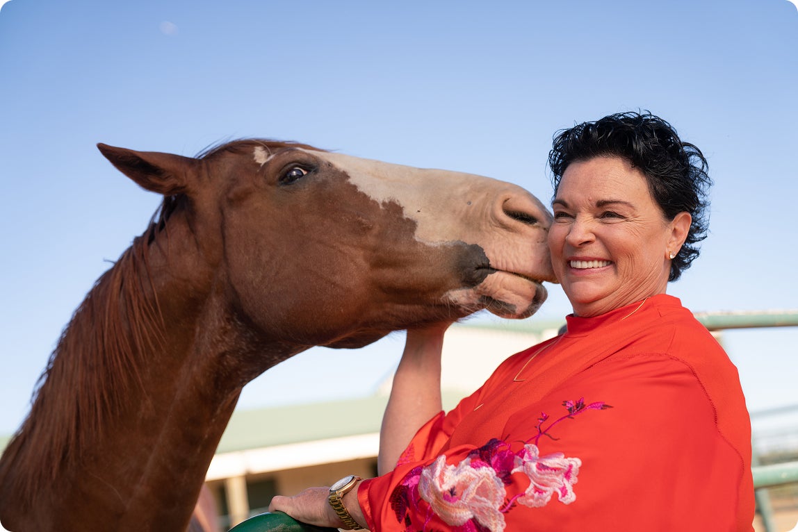 A ClearChoice patient smiling while interacting with a horse outdoors, representing confidence and the ability to enjoy favorite activities after dental implant treatment.
