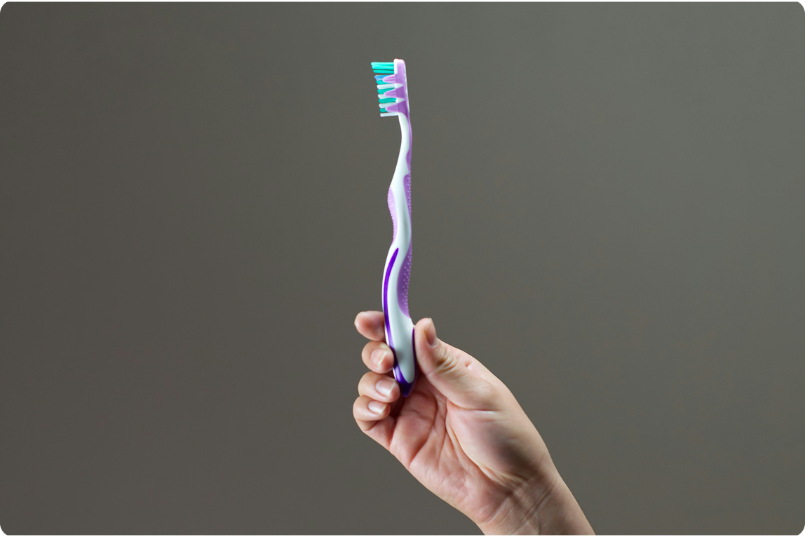 hand holding a toothbrush against a neutral background, representing daily oral hygiene and proper cleaning for dental implants and overall oral health