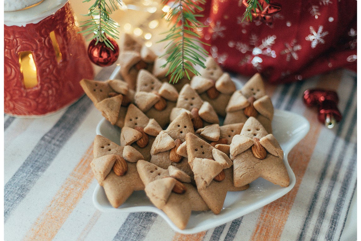 A plate of homemade Christmas tree–shaped cookies decorated with almonds, surrounded by holiday décor and warm lighting.