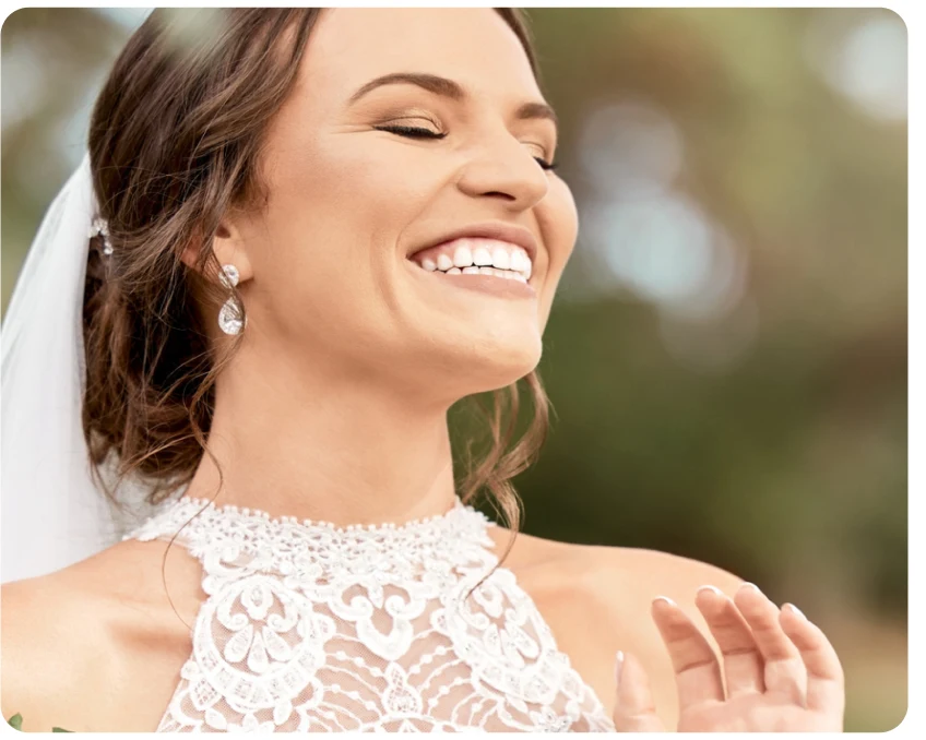 A bride in a lace wedding dress and veil, smiling with eyes closed.