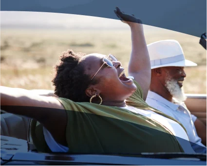 An older couple smiles as they drive in a convertible.