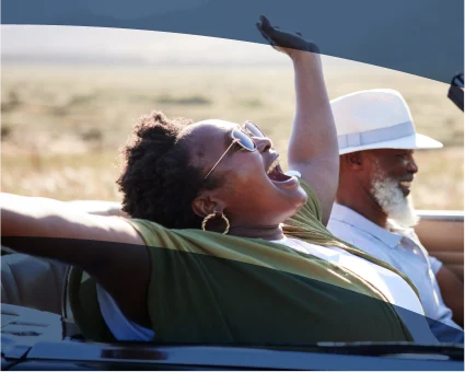 An older couple smiles as they drive in a convertible. 