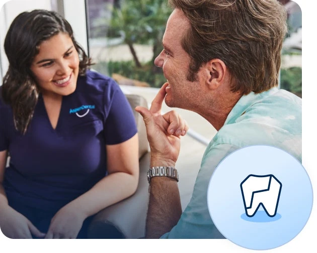 A dental professional in a navy scrubs talks to a seated man who points at his teeth. A circular badge at the bottom right with a cracked tooth icon depicts veneers can correct several dental issues.