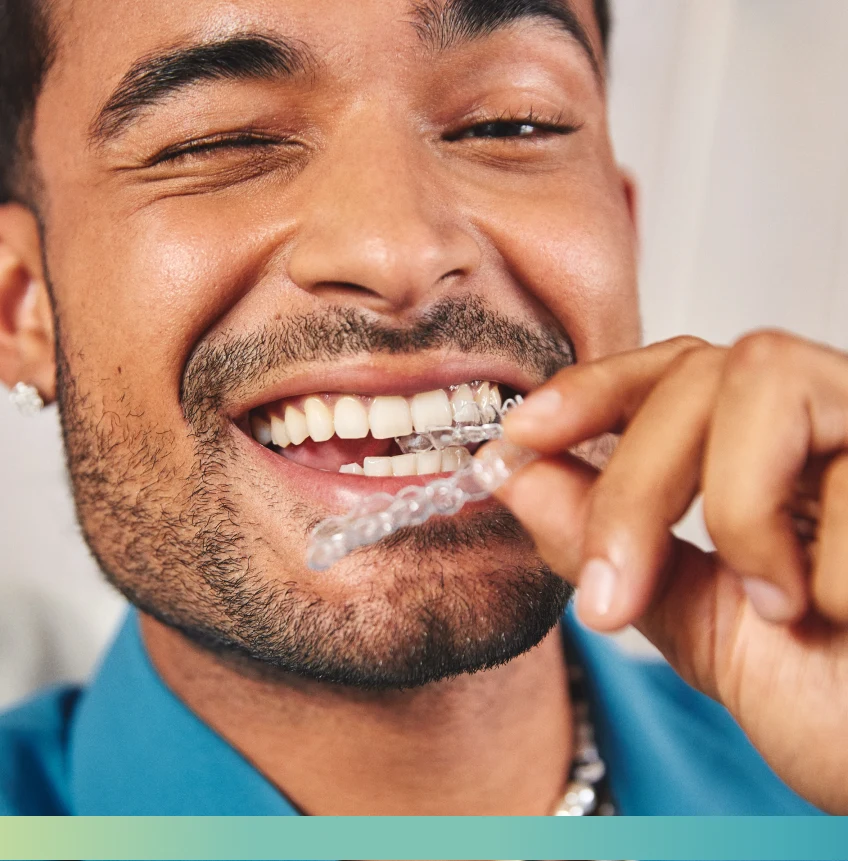 A person wearing a blue shirt holds a clear dental aligner near their teeth, smiling and winking.