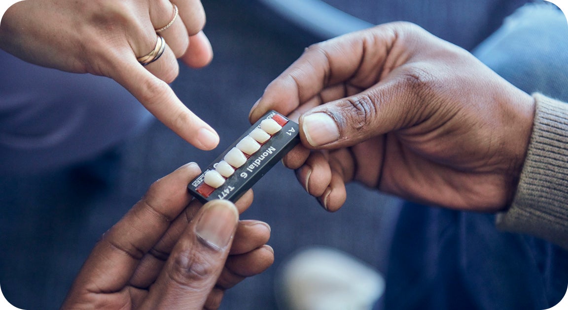 A close-up of hands reviewing a tooth shade guide, illustrating the personalized planning process patients undergo with dental implants treatment.