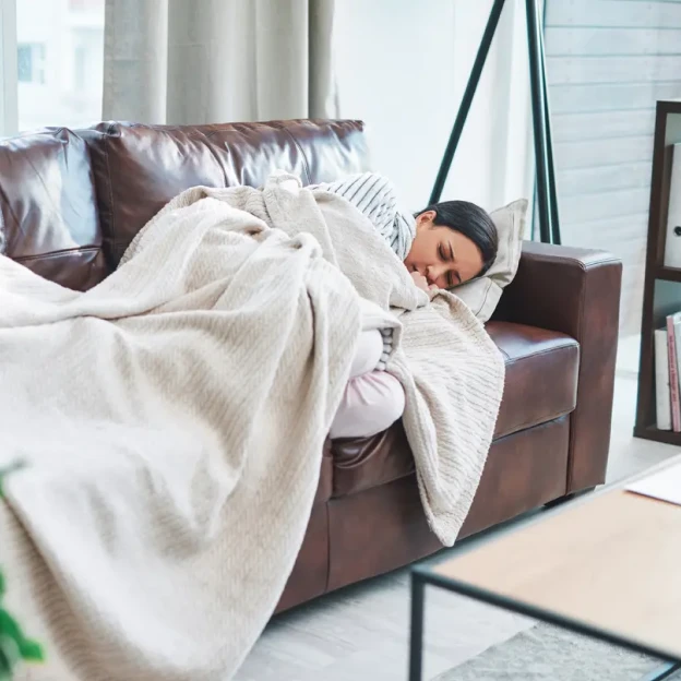 A woman sleeps on a couch under a blanket. 