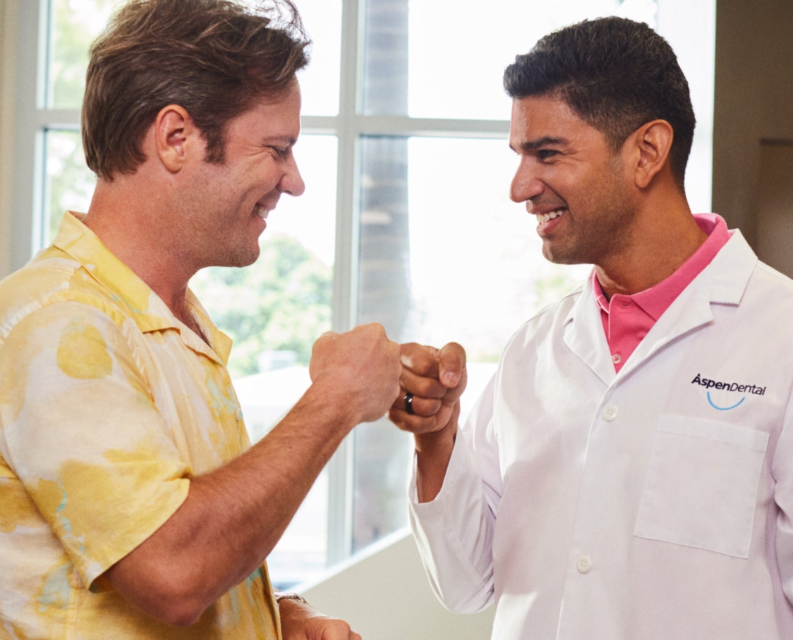 A friendly interaction between an Aspen Dental dentist and a patient, exchanging a fist bump and smiling, symbolizing trust and satisfaction with the dental care experience.