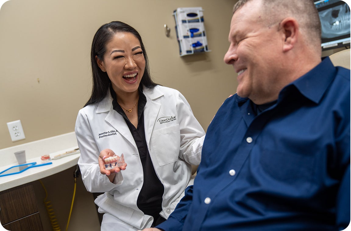 A prosthodontist smiles warmly while speaking with a patient during a dental implant consultation. This moment reflects supportive care and a patient-first philosophy.