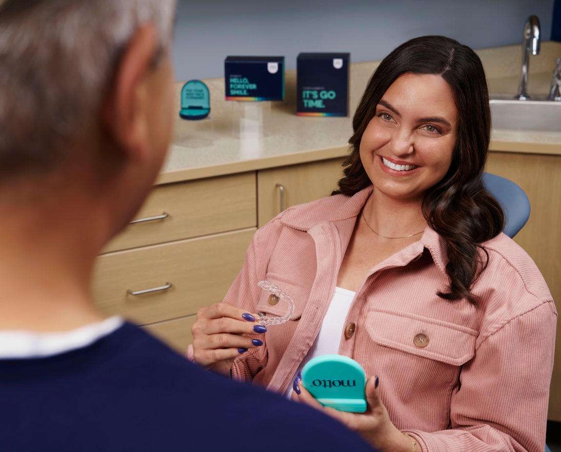 Happy patient sitting in the dental chair with her Motto Clear Aligners, receiving in-person provider care as she progresses toward a straighter smile.