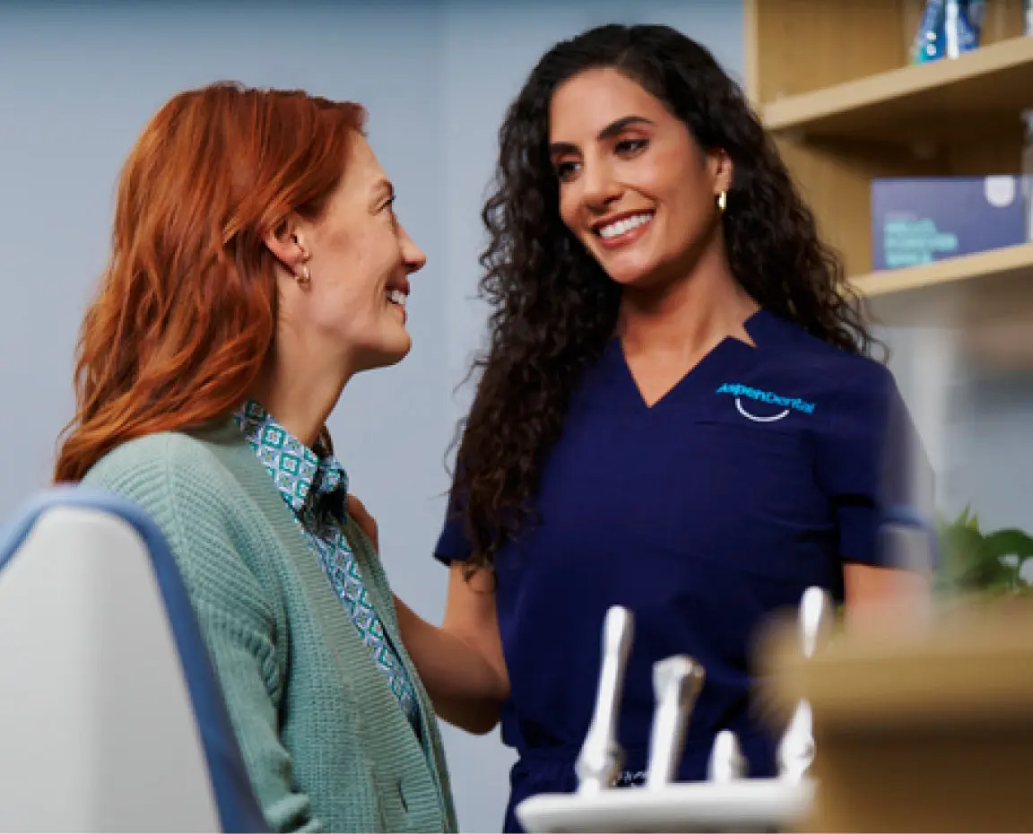An Aspen Dental doctor in blue scrubs is talking to another woman