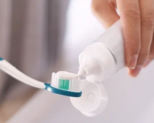 A hand squeezes toothpaste onto a toothbrush. 