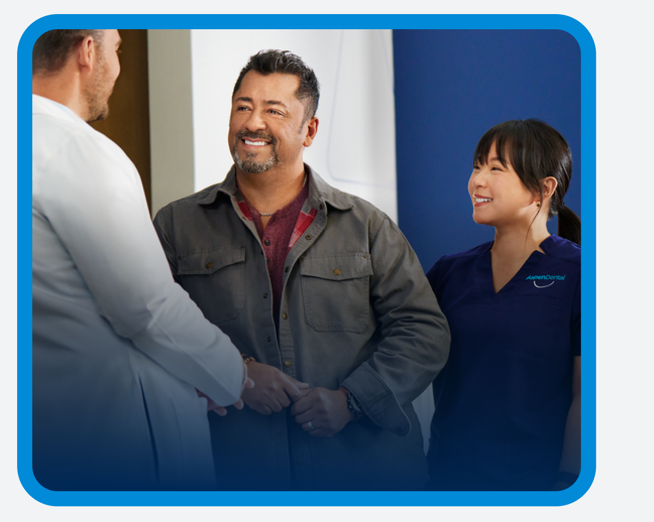 Un hombre con una chaqueta gris sonriendo mientras habla con un dentista y un asistente dental de Aspen Dental.