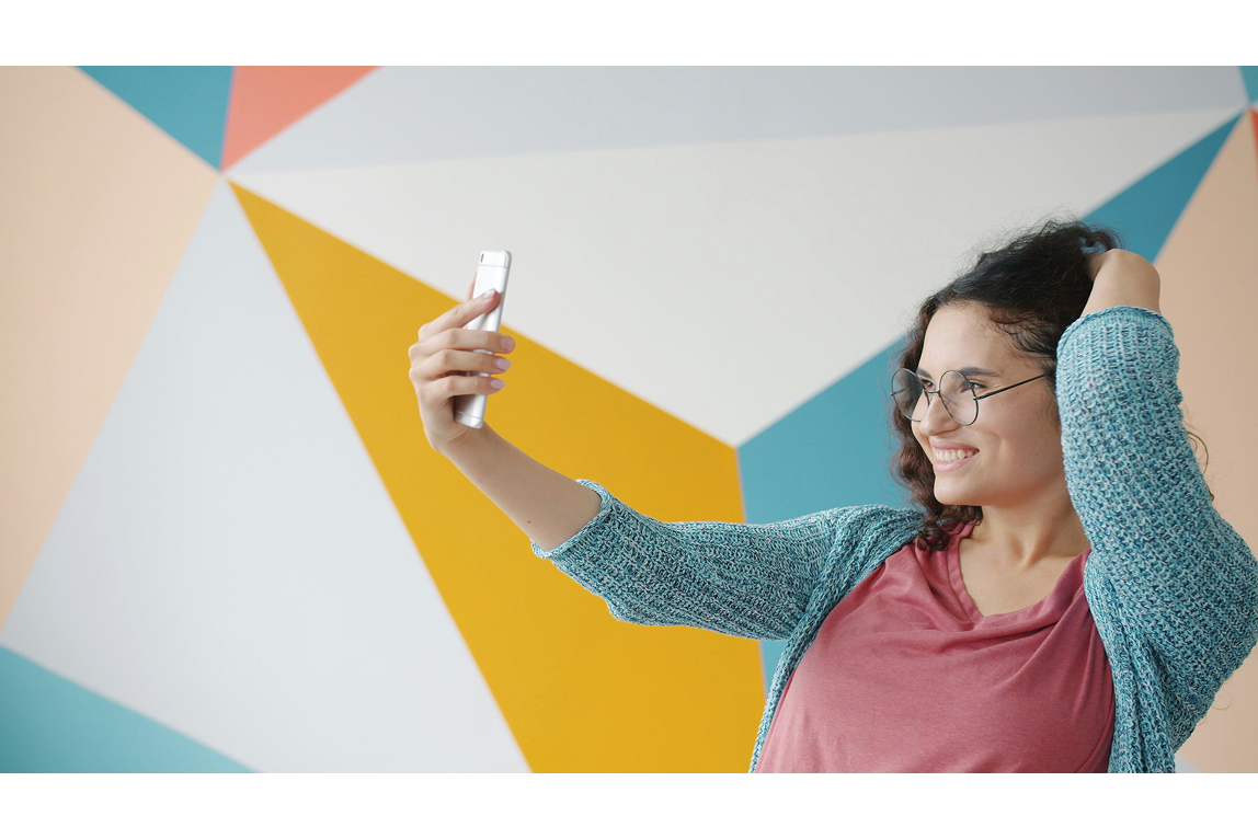 woman taking a selfie and smiling with a smartphone, representing social media beauty standards and the difference between everyday smiles and a Hollywood smile in cosmetic dentistry