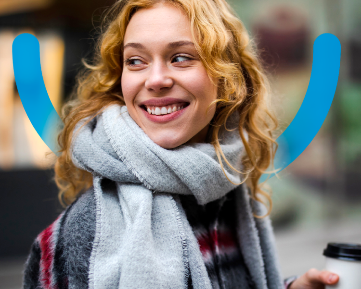 A smiling woman in a scarf holding a coffee cup with the Aspen Dental blue smiley face graphic underlaid.
