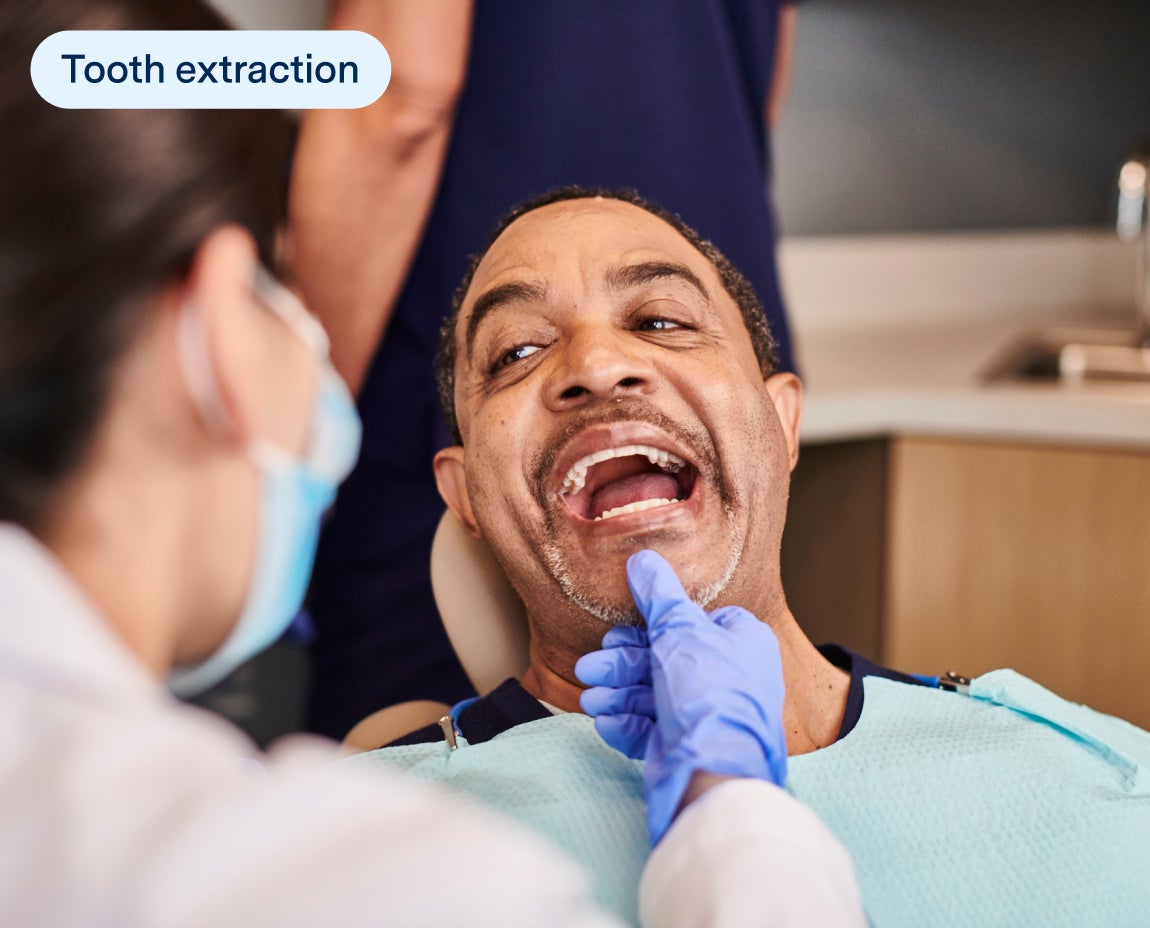 Male patient in a dental chair preparing for a tooth extraction procedure with a dentist in protective gear examining his mouth.