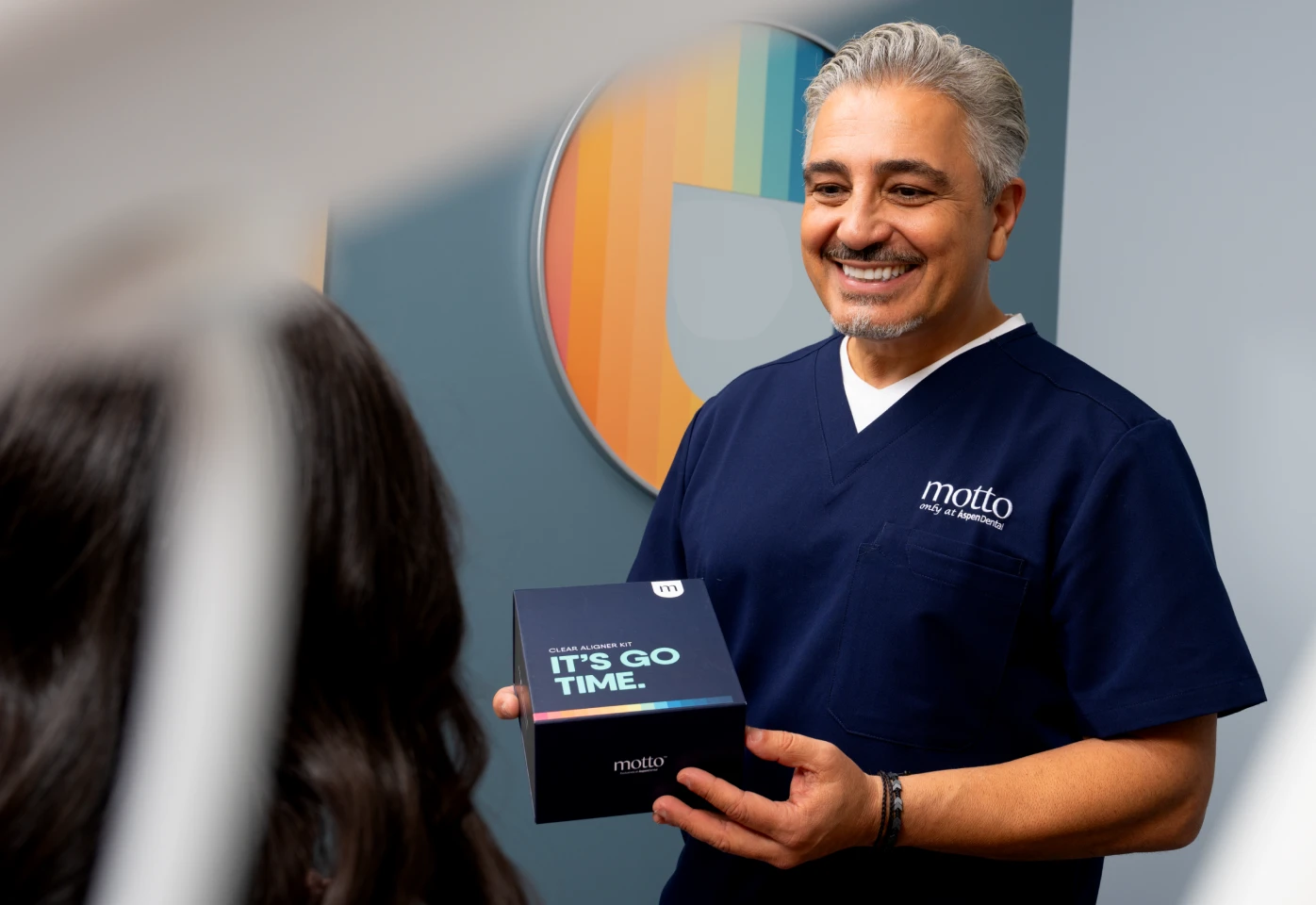 Dr. Attaii smiles while handing a Motto clear aligners box to a patient.