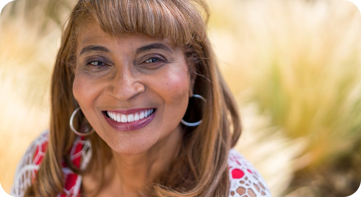 A woman smiles confidently outdoors, representing a patients who’s transitioned from dentures to dental implants and regained comfort, function, and aesthetics after years of removable denture use.