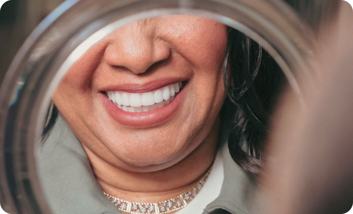 A ClearChoice patient smiling confidently into a mirror with her brand new dental implants.